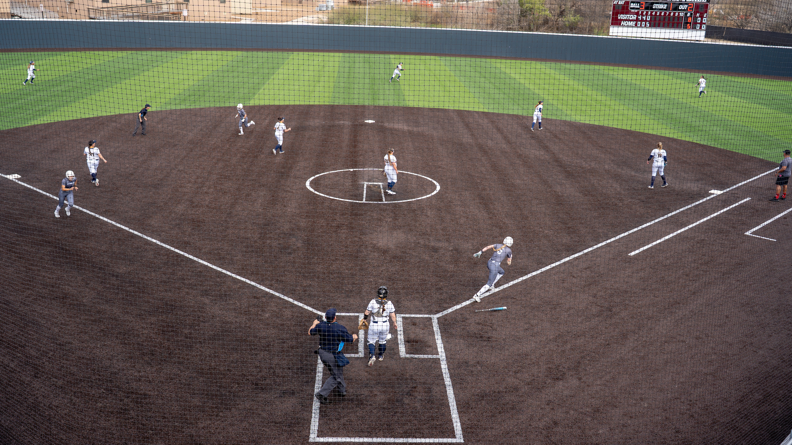 Softball field during game, with players running between bases.