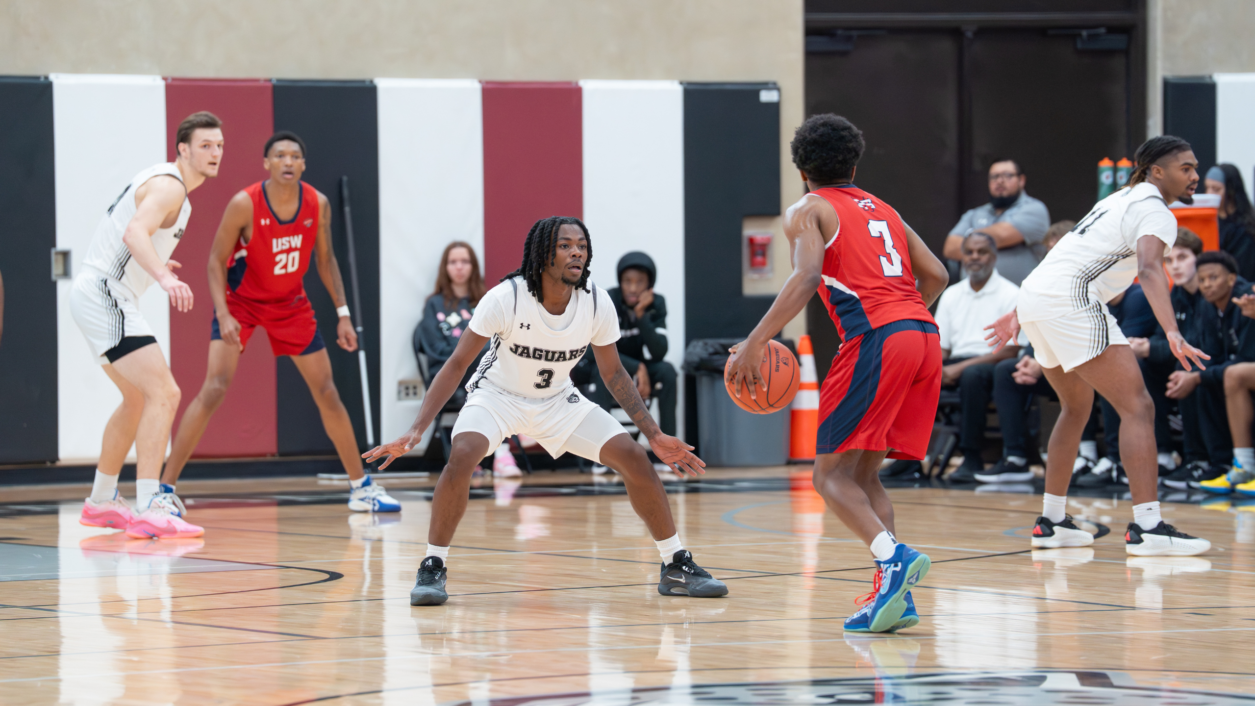 Men's Basketball player with jersey number 3 guarding the basket from the opponent trying to dribble past.